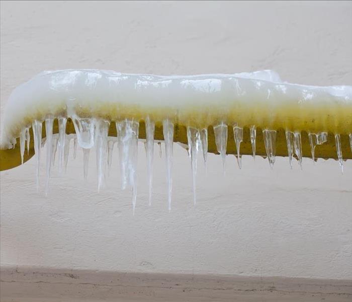Icicles hanging from a frozen water jets, tube, yellow pipe. aged wall background. winter time concept 